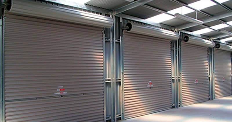 quatro portões de garagem rolantes em metal branco em ambiente industrial